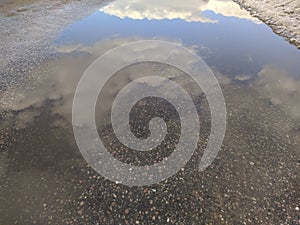 reflection of blue sky and white clouds in a puddle.