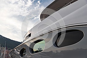 Reflection of a boat on a glossy surface of a huge yacht at sunset, the chrome plated handrail, megayacht is moored in