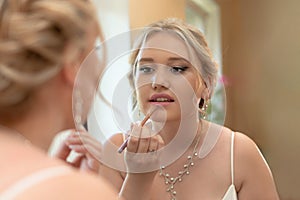 Reflection of bride in mirror who corrects her makeup,paints her lips with lipstick,concept of a wedding,a marriage