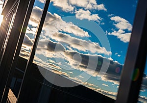 Reflection of a bright blue sky with scattered white clouds is captured on the glass surface of a