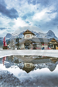 Reflection of a building with mountains in a puddle in the Village Square in Canmore, Alberta
