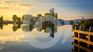 Reflection of buildings and leafy trees on a still mirror lake captured at sunset