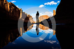 Reflection in calm lake in the desert of Southern Utah. Reflection of a man standing by the pond as well as red rock towers and
