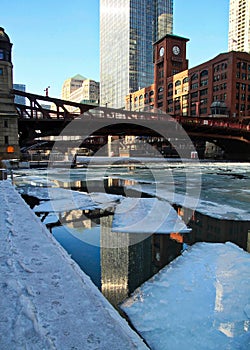 Reflection of city buildings on Chicago River with ice chunks.