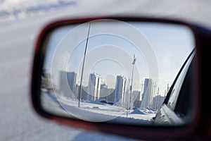 Reflection of cityscape in rear-view mirror of the car on a frosty winter day