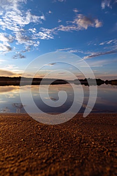 Reflection of clouds and twilight sky over the clear water surface, vertical shot