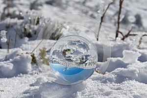 Reflection in a crystal ball of a mountain landscape with snow on a sunny day and blue sky.