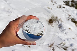 Reflection in a crystal ball of a mountain landscape with snow on a sunny day and blue sky.