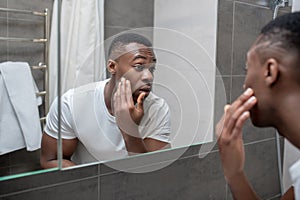 Dark-skinned young handsome man looking at himself in the mirror