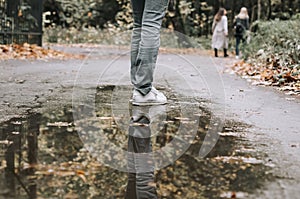 Reflection of girl wearing white shoes in water puddle. Unknown woman passed small puddle. reflection of female legs in a puddle