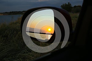 Reflection of landscape with beautiful sunset over calm river in car side view mirror, closeup