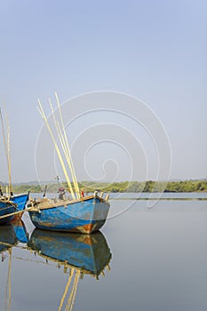 Reflection of a large blue fishing boat anchored near the shore on a smooth surface of water against the background of a river and