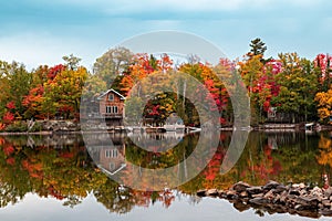 Reflection of a leafy forest in fall colors, autumn foliage and a wooden house on a mirror lake