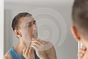 Reflection of man in mirror removing hair above upper lip. Morning routine in bathroom. View from behind the shoulder