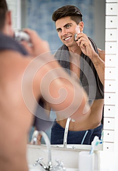 Reflection of man in mirror shaving with electric shaver