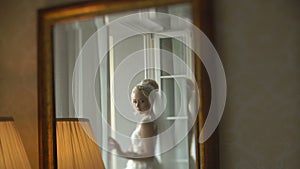 Reflection in the mirror of the adorable blonde bride in the stylish wedding dress, veil and with wonderful make-up