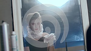 Reflection in mirror of gorgeous young actress with red and white make-up adjusting hairdo at backlit. Portrait of