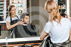 Reflection in mirror of hairdresser doing hairstyle to handsome client