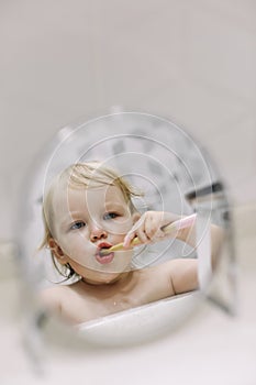 reflection in the mirror of a little funny girl brushing her teeth