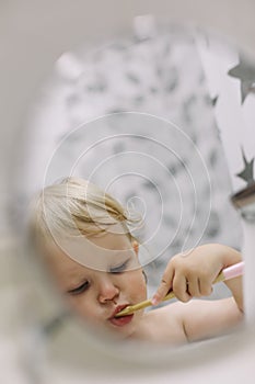 reflection in the mirror of a little funny girl brushing her teeth