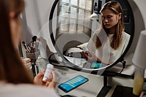 Reflection in mirror of stressed teenage girl looking at bottle of pills in her hands