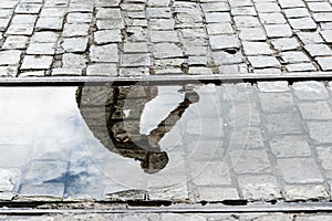 Reflection of person and bicycle in a puddle of rainwater in the river