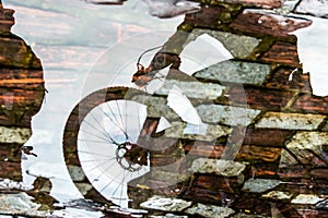 Reflection of person and bicycle in a puddle of rainwater in the river
