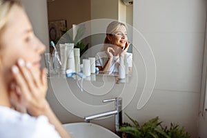 Reflection of pretty young blonde female in mirror in bathroom. Close up. Skincare routine.