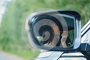 Reflection in rear view mirror of a woman applying lipstick while sitting in the car