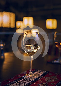 Reflection of the restaurantâ€™s light rays and the surrounding space in a glass of white wine standing on a restaurant table