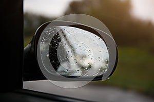 The reflection of road in the side view mirror with raindrops. Travel concept. Bad weather and grey sky