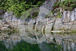 Reflection of rocks of cliff face in calm water of cove in Broughton Archipelago