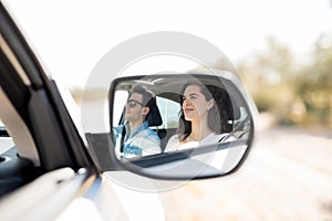 Reflection in side view mirror of couple traveling by car