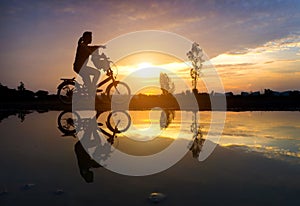 Reflection Silhouette of mother with her toddler on bicycle against the sunset and lens flare.