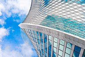 Reflection of sky and clouds in glass spiral, wave with bend facade windows of financial skyscrapers.