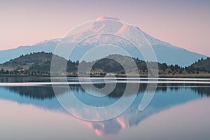 A reflection of snow capped Mount Shasta in a clear water in lake  at sunrise in California State, USA.  Mount Shasta is a volcano photo