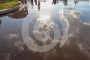 Reflection of the sun and blue sky with clouds in a puddle.