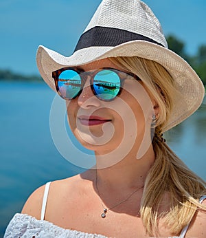Reflection in sunglasses. Girl in a white straw hat