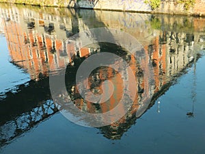 Reflection of a sunlit house and a bridge across the Naviglio Grande canal in Milan