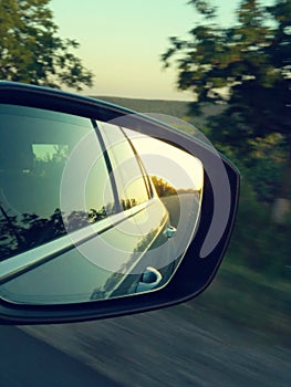 Reflection of sunny road at the car side mirrow. Rear view mirror reflection on sun down