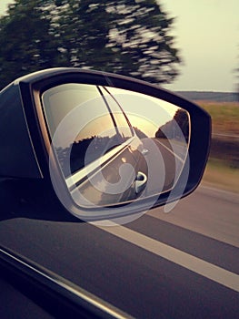 Reflection of sunny road at the car side mirrow. Rear view mirror reflection on sun down