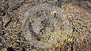 Reflection of sunshine on water with pebble stone on ground. Clean water surface with moving wave of golden reflecting sunlight.