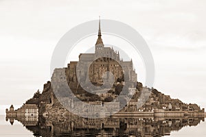 Reflection on the water of abbey of Monte Saint Michel in Northern France with sepia toned photo
