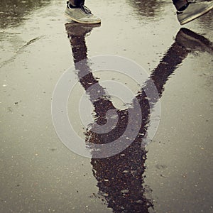 Reflection in the wet asphalt. Walking teenager.