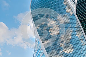 Reflection of white clouds and blue sky in glass wall of modern skyscraper