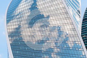 Reflection of white clouds and blue sky in glass wall of modern skyscraper