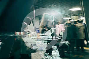 Reflection in the window at passengers and their luggage walking along the boarding corridor of the aircraft from the