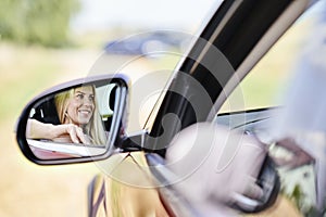 Reflection in wing mirror of smiling woman driving car