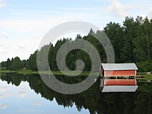 Reflection of a wooden cottage and the trees on a calm and tranquil lake captured in Finland