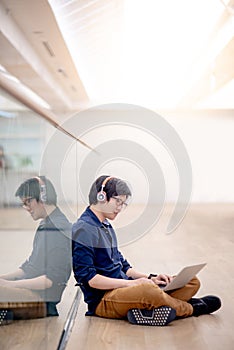 Young Asian business man listening to music while using laptop